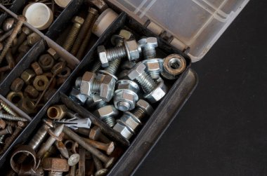 İçinde çeşitli metal bağlayıcılar olan plastik bir kutu. Eski ve yeni cıvatalar, fındıklar, vidalar ve vidalar. Fotokopi alanı olan endüstriyel arka plan. Bir açıyla üstteki görünüm.
