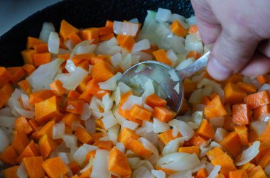 Erkek el kızartma tavasında doğranmış beyaz soğan ve çiğ havuç karıştırıyor. Kızartma işlemi çiğ soğan dilimleri ve yakın plan havuç. Bir açıdan üstten bak. Seçici odak.
