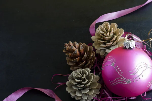 Christmas festive background. Three pine cones and a pink glass Christmas ball on a black background. Festive mood. Copy space.