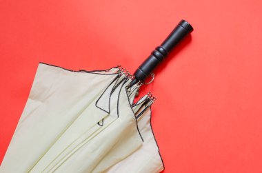 Mercan zemin üzerinde zarif, açık bej bir şemsiye. Kara saplı yağmur ve rüzgar koruma aksesuarı. Bir açıdan üstten bak. Boşluğu kopyala