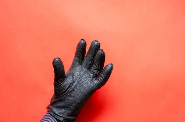Male hand in a leather glove on coral background. The man is showing his hand in a black leather glove. Side view. Selective focus.