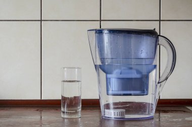 Mutfak tezgahında silikon kartuşlu su filtresi. Sıvının minerallerle doyması için silikon kartuş. Plastik sürahi ve bir bardak saf su. Su iç..