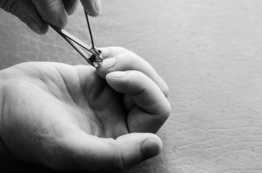 Orta yaşlı beyaz bir adam kendi tırnaklarını kesiyor. Erkek avuçlarında tırnak makası. Sağlık ve hijyen. Yakın plan. Siyah beyaz bir fotoğraf..