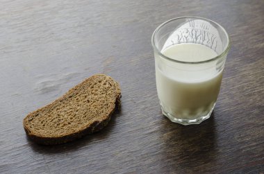 Yarım bardak kefir ve bir dilim çavdar ekmeği. Mayalanmış sütlü cam bardak. Basit sağlıklı yiyecekler. Bir açıyla üstteki görünüm.