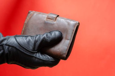 Elindeki siyah deri eldiven kahverengi cüzdanı uzatıyor. Erkek eli cüzdanı satın almak ya da hırsızlık konseptini ödemek için tutar. Yan görüş. Seçici odak.