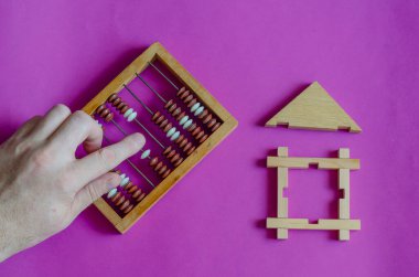 Erkek el, leylak arka plandaki oyuncak ahşap evin yanında bir abaküs hesaplar. İpotek veya borç verme kavramı gayrimenkul tarafından güvence altına alınmıştır. Yukarıdan görüntüle.