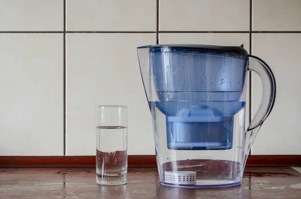 Water filter jug with silicon cartridge inside on the kitchen counter. Silicon cartridge for saturation of liquid with minerals. Plastic jug and glass of purified water. Drink water.