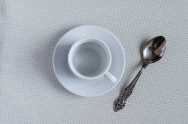 Beyaz desenli arka planda çay tabağı ve kaşıkla dolu boş beyaz kahve fincanı. Sıcak içecekler için seramik tabaklar. Klasik bir tarz. Bir açıyla üstteki görünüm.