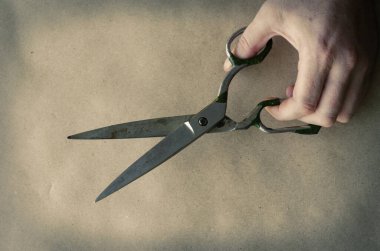 Yaşlı bir terzi makası, yetişkin bir beyaz adamın elinde. El, eski bir el aletini tutuyor. El işçiliği. El sanatları. Bir açıyla üstteki görünüm.