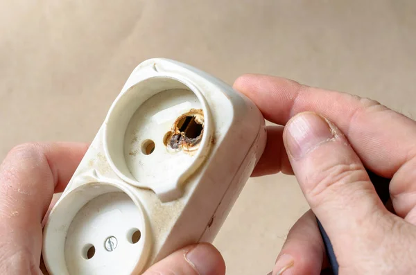 Bir elektrikçi elektrik prizinin yandığını gösteriyor. Erkek eli kısa devreden sonra beyaz uzatma kablosu. Elektrik güvenliği.