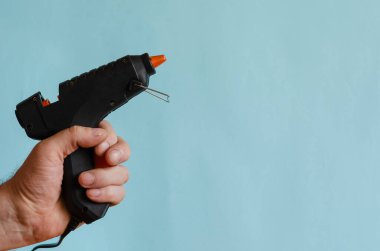 Erkek elinde tutkal termometresi. Nesneleri yapıştırıcı çubuklarıyla yapıştırmak için elektrikli bir cihaz. Avrupa ırkının orta yaşlı adamı. Çalışma ve yaratıcılık için elde taşınabilir elektrikli araçlar