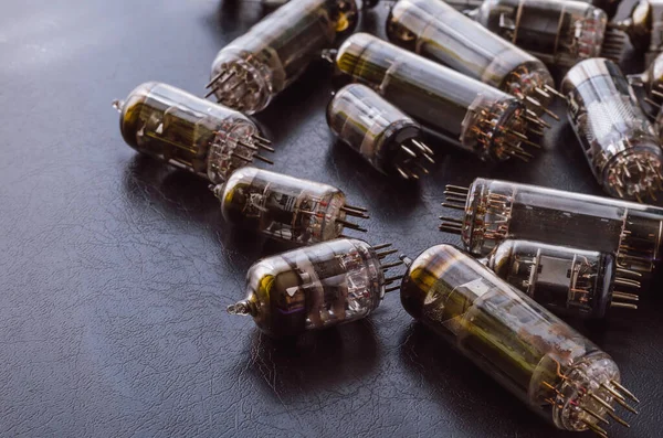 Random vacuum tubes on a black background. A group of radio tubes of different sizes and purposes. Shooting at eye level. Selective focus.