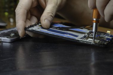 Özel bir atölyede akıllı telefonu tamir etme süreci. Erkek el vidayı tornavidayla söker. Servis bakımı. Seçici odak.