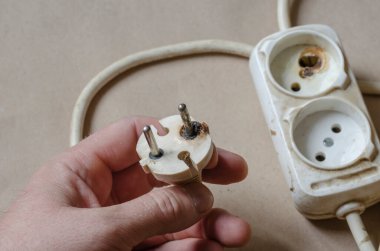 Bir elektrikçi bir elektrik prizinin yandığını gösteriyor. Erkek eli kısa devreden sonra beyaz uzatma kablosu. Elektrik güvenliği.