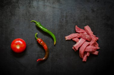 Çiğ biftek şeritleri, olgun domates ve siyah üzerine acı biber kabukları. Çiğ et fileto ve çiğ sebze servisi. Yukarıdan bak. Boşluğu kopyala.