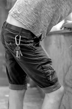 Genç adam dirsekleriyle taş çitin üzerinde dikiliyor. Anahtarlar kemerde asılı. Yaşam tarzı. Yan görüş. Seçici odaklanma. Tek Renkli