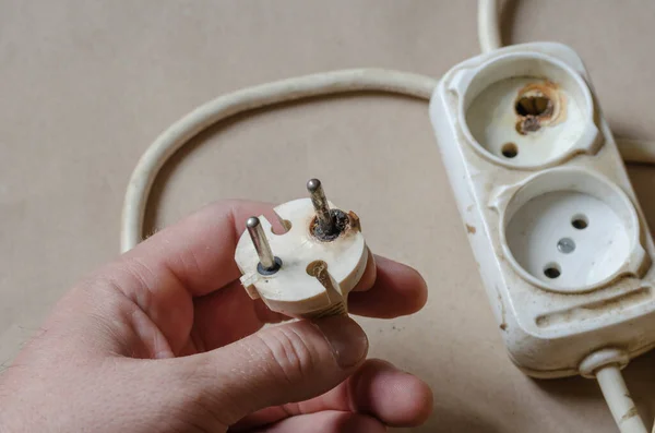 Bir elektrikçi bir elektrik prizinin yandığını gösteriyor. Erkek eli kısa devreden sonra beyaz uzatma kablosu. Elektrik güvenliği.