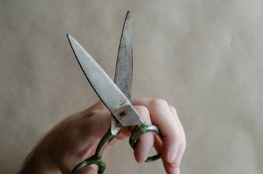 Yaşlı bir terzi makası, yetişkin bir beyaz adamın elinde. El, eski bir el aletini tutuyor. El işçiliği. El sanatları. Bir açıyla üstteki görünüm.