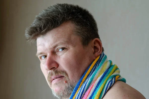 Mature man with rainbow-colored bath towel over his shoulders. Middle-aged Caucasian man with beard and mustache looks confidently into the camera.