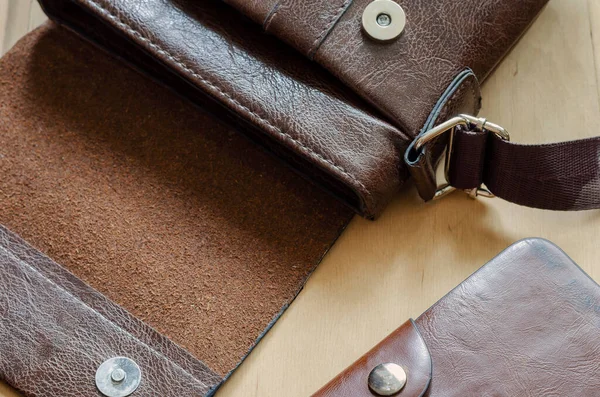 Small leather bag and wallet on wooden table. Open bag and brown leather wallet. Top view at an angle. Selective focus.