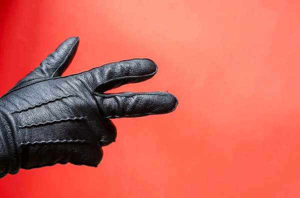 Male hand in leather glove gestures against coral background. Man shows his hand in black leather glove. Side view. Selective focus.