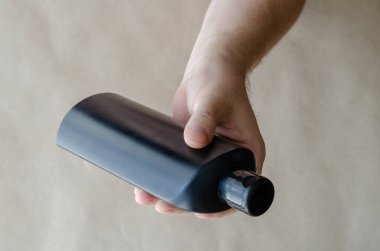 Beyaz adam elinde siyah şampuan şişesi ya da duş jeli tutuyor. Elinde siyah plastik şişe olan orta yaşlı bir adamın eli. Kişisel hijyen. Seçici odak.