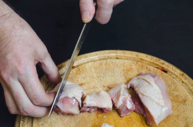 Bir adam doğrama tahtasındaki tavuğu bıçaklıyor. Yetişkin bir Avrupalı adamın eli çiğ kümes hayvanlarını parçalara ayırıyor. Yemek pişirmek. Seçici odak.