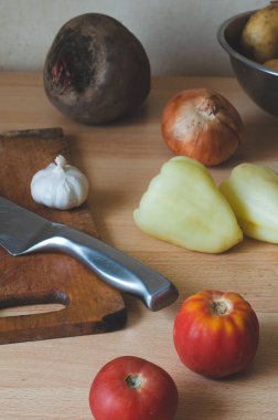 Çiğ, soyulmamış sebzeler, mutfak masasında tahta ve bıçak. Domates, sarımsak, dolmalık biber ve pancar. Öğle yemeği malzemeleri. Seçici odak.