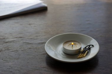 Küçük yanan bir mum ve bir grup yanmış kibrit masanın üstünde bir fincan tabağında. Korunan mum bir anı sembolüdür. Yan görüş. Uzayı kopyala Seçici odak.