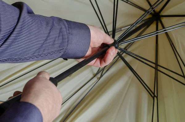 Male hands open the umbrella. Man in blue striped shirt straightens beige umbrella. Caucasian, middle-aged. Shooting from behind. Selective focus.