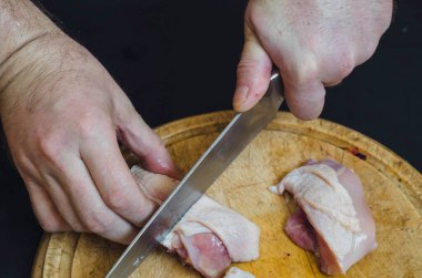 Bir adam doğrama tahtasındaki tavuğu bıçaklıyor. Yetişkin bir Avrupalı adamın eli çiğ kümes hayvanlarını parçalara ayırıyor. Yemek pişirmek. Seçici odak.