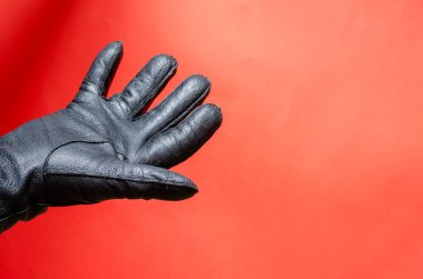 Mercan arka planında deri eldivenli bir erkek el hareketi. Adam elini siyah deri eldivenle gösteriyor. Yan görüş. Seçici odak.
