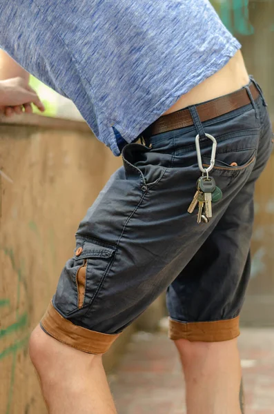 Genç adam dirsekleriyle taş çitin üzerinde dikiliyor. Anahtarlar kemerde asılı. Yaşam tarzı. Yan görüş. Seçici odak.