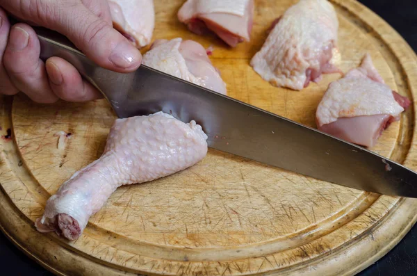 Bir adam doğrama tahtasındaki tavuğu bıçaklıyor. Yetişkin bir Avrupalı adamın eli çiğ kümes hayvanlarını parçalara ayırıyor. Yemek pişirmek. Seçici odak.