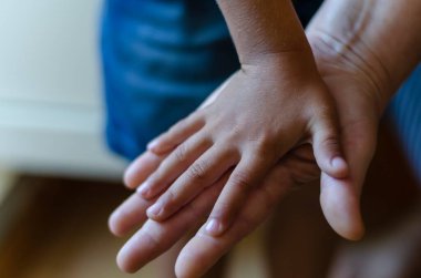 Bir çocuğun eli yetişkin bir avucunun üzerindedir. Küçük bir çocuğun avuç içi açık bir yetişkin avucunu örter. Yakın plan. Seçici odak.