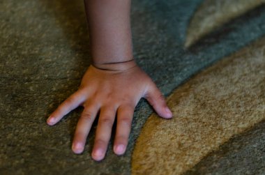 İçerideki yeşil halıya bir çocuğun elini yakın plan çek. Anaokulu çocuğu elini yere koydu. Bir açıdan üstten bak. Seçici odak.