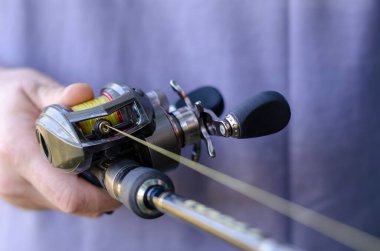 Close-up of male hand with a fishing rod and  baitcasting reel. Caucasian man is fishing with casting rod. Sports and recreation. Selective focus. clipart