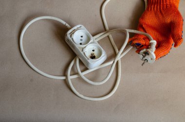 Koruyucu turuncu eldiven takan el yangından sonra fiş tutuyor. Kısa devreden sonra beyaz güç şeridi. Elektrik güvenliği.