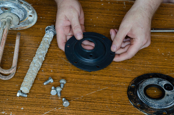 Hands of an adult male hold the rubber gasket for the water heater. Commercial home electric water heater repair services. Service and warranty service for household appliances.