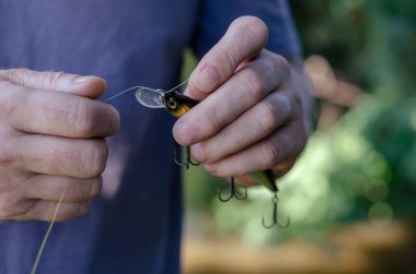 Yetişkin bir adam plastik yalpalayıcıyı misinaya bağlar. Yırtıcı balık yakalamak için yapay yem. Aktif yaşam tarzı. Seçici odak.