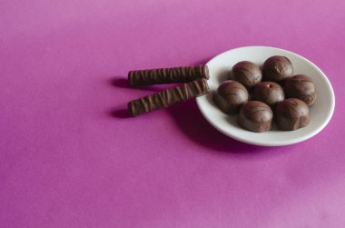 Beyaz tabakta pembe arka planda rastgele çikolatalar. Çeşit çeşit şekerlemeler var. Tatlı ikramlar. Seçici odak.