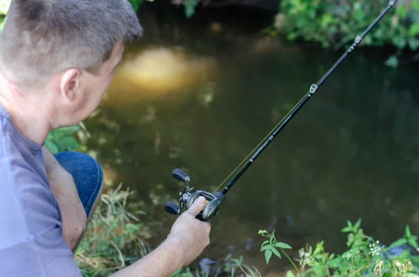 大人の男は森の川のほとりで捕食魚をキャッチします 彼の手にロッドを持つ短髪の漁師 積極的なライフスタイル 選択的焦点 — ストック写真