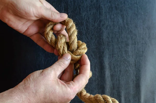 Male hands tie a knot on a rope. A mature man with a thick rope in his hand. Active lifestyle. Selective focus.