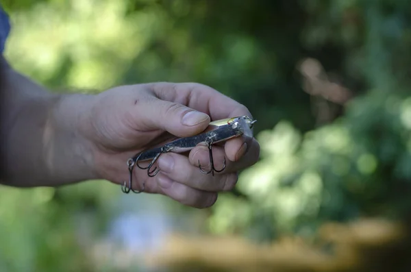 男の手は3つのフックを持つプラスチック製のぐらつきを保持します 捕食魚を捕まえるための人工餌 積極的なライフスタイル 選択的焦点 — ストック写真