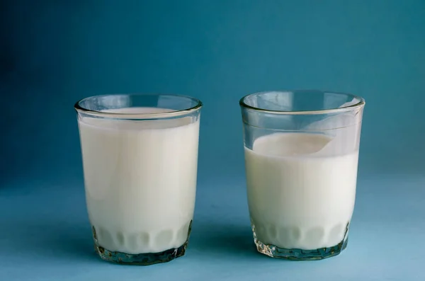 两杯蓝色底色的玻璃杯 一杯满满一杯的发酵牛奶和一杯半杯的发酵牛奶 喝一些对消化有益的东西 复制空间 — 图库照片