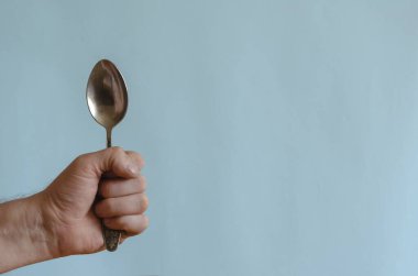 Yetişkin bir erkeğin elinde metal bir kaşık var. Sol elinde paslanmaz çelik kaşık var. Avrupa ırkının orta yaşlı adamı. Çatal bıçak takımı.