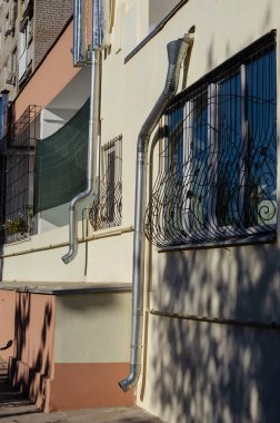 İndirme boruları ve pencere parmaklıkları olan binanın ön cephesi. Çok katlı bir binanın ilk katı. Şehir mimarisi. Seçici odak.