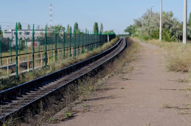 Demiryolunu dikenli tellerle metal bir çit boyunca bükün. İstasyon peronu çimlerle kaplıydı. Ön plana odaklan. Hiç kimse olmadan.