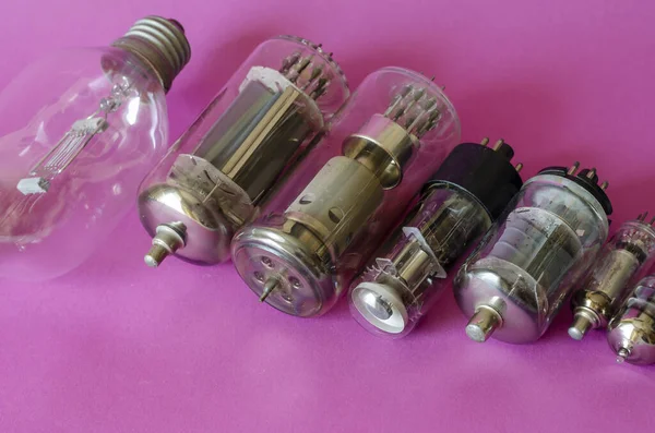 Various vacuum tubes on a pink background. A group of random radio tubes. Types of obsolete electrical parts. Selective focus.
