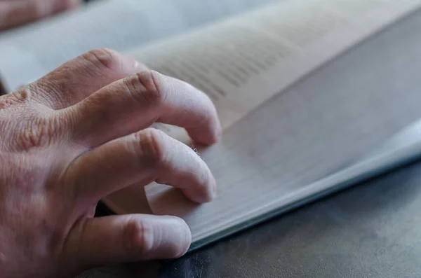 Mature male hand from above on an open book. Thick hardcover book. Male hand with a book on a black table. Selective focus.